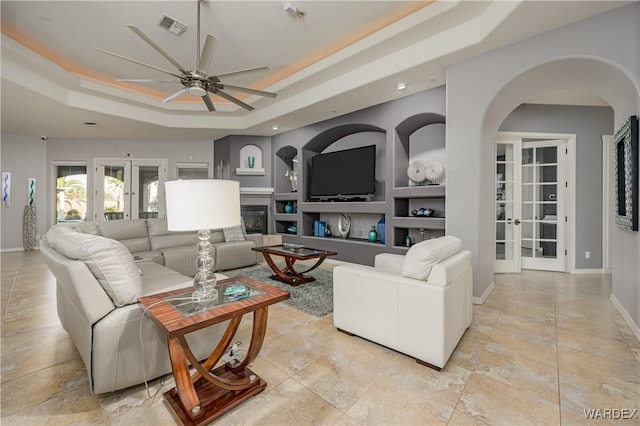 living room featuring built in shelves, visible vents, a glass covered fireplace, and french doors