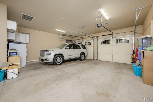 garage featuring freestanding refrigerator, visible vents, and a garage door opener