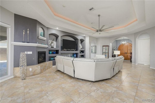 living area featuring built in features, a tray ceiling, arched walkways, visible vents, and a tiled fireplace