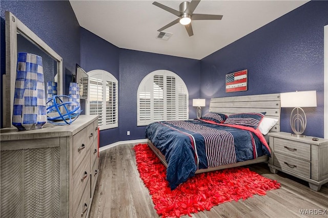 bedroom with light wood-style floors, visible vents, a textured wall, and baseboards