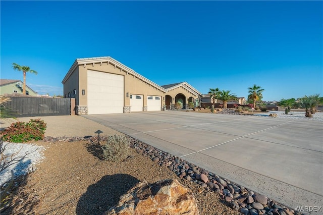 view of front of house with a garage, concrete driveway, stone siding, fence, and stucco siding