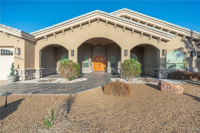 mediterranean / spanish-style house with stone siding, a tile roof, and stucco siding