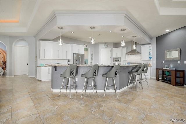 kitchen with wall chimney exhaust hood, hanging light fixtures, and white cabinets