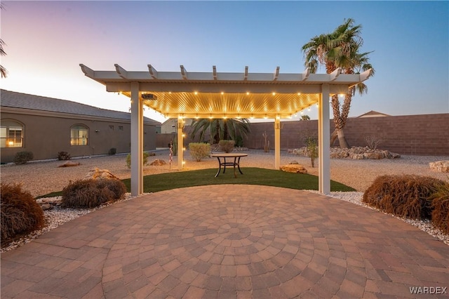 patio terrace at dusk featuring fence and a pergola