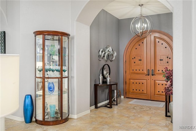 foyer entrance featuring arched walkways, baseboards, and an inviting chandelier