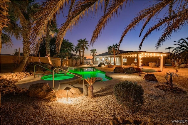 pool at dusk with a pool with connected hot tub, fence, and a patio