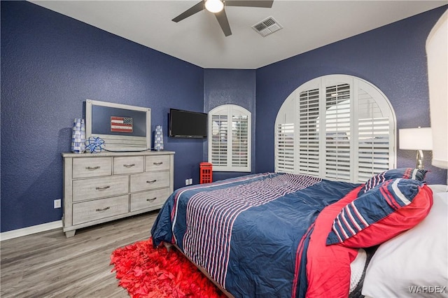 bedroom featuring baseboards, visible vents, a textured wall, ceiling fan, and wood finished floors