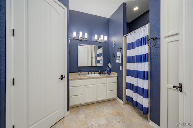 full bath featuring a textured wall, baseboards, and vanity