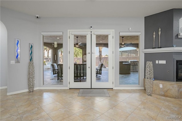 doorway to outside featuring french doors, a fireplace, light tile patterned floors, ceiling fan, and baseboards