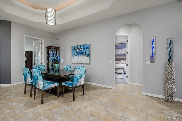 dining room featuring arched walkways, baseboards, and a tray ceiling