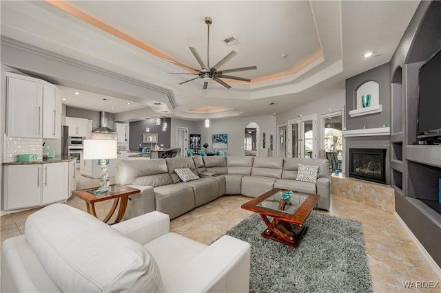 living room with visible vents, a raised ceiling, a ceiling fan, a glass covered fireplace, and recessed lighting