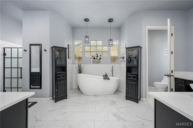 full bath with toilet, a soaking tub, marble finish floor, vanity, and tile walls