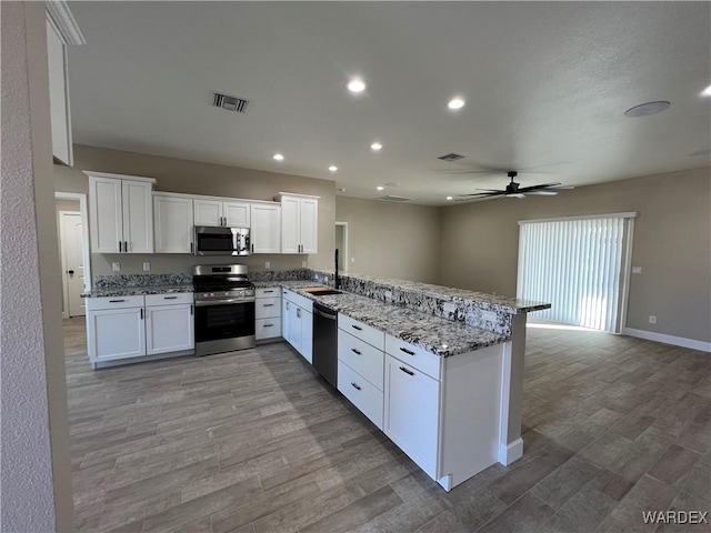 kitchen with visible vents, a peninsula, light stone countertops, stainless steel appliances, and white cabinetry