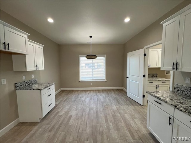 kitchen featuring white cabinetry, hanging light fixtures, light wood-style flooring, and light stone countertops