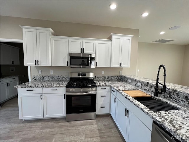 kitchen with appliances with stainless steel finishes, a sink, light stone counters, and white cabinets