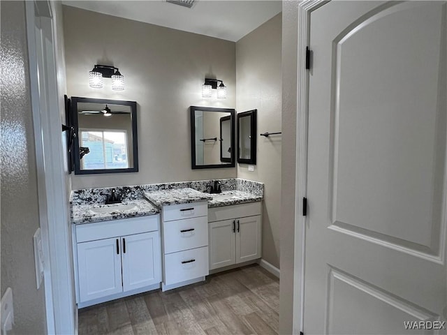 bathroom featuring ceiling fan, double vanity, wood finished floors, and a sink