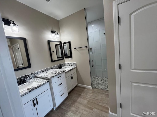 bathroom featuring double vanity, a shower stall, baseboards, and a sink