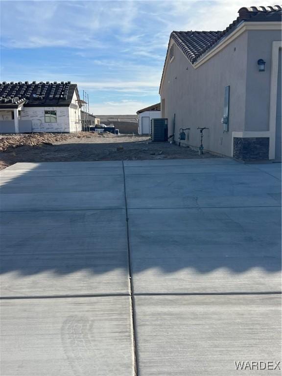 view of side of property with driveway, central air condition unit, and stucco siding