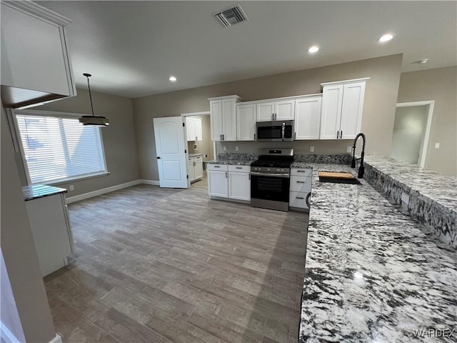 kitchen featuring stainless steel appliances, a sink, white cabinets, light stone countertops, and decorative light fixtures