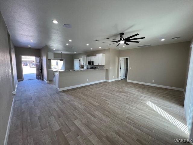 kitchen with white cabinets, open floor plan, wood finished floors, a peninsula, and light stone countertops