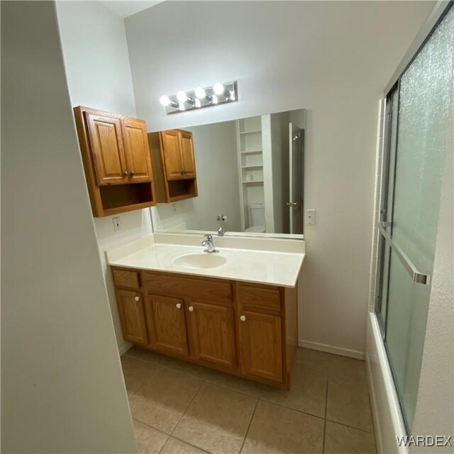 bathroom featuring shower / bath combination with glass door, toilet, vanity, tile patterned flooring, and baseboards