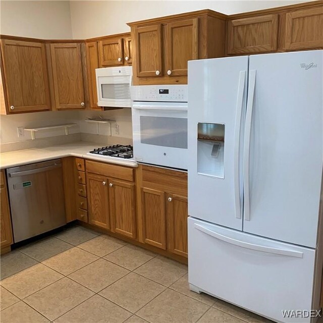 kitchen featuring brown cabinets, white appliances, light tile patterned floors, and light countertops