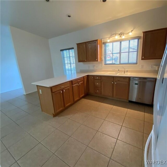 kitchen featuring light countertops, stainless steel dishwasher, brown cabinetry, a sink, and a peninsula