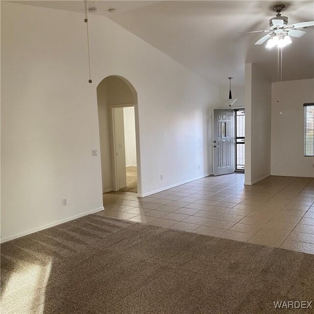 empty room with arched walkways, light tile patterned floors, light colored carpet, ceiling fan, and high vaulted ceiling