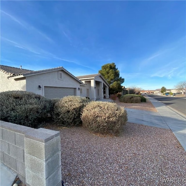 view of side of home featuring a garage, a tile roof, and stucco siding