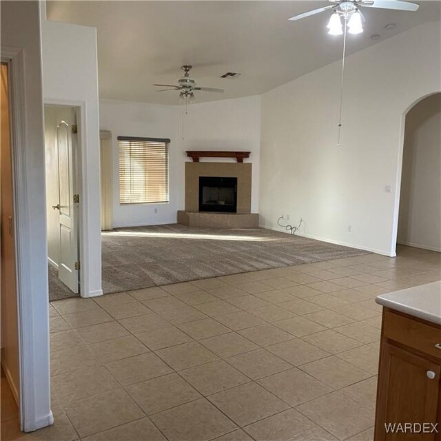 unfurnished living room with ceiling fan, a fireplace with raised hearth, light tile patterned floors, arched walkways, and visible vents