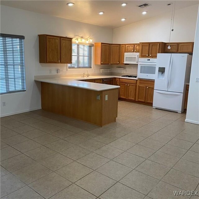 kitchen with a peninsula, white appliances, visible vents, light countertops, and brown cabinets