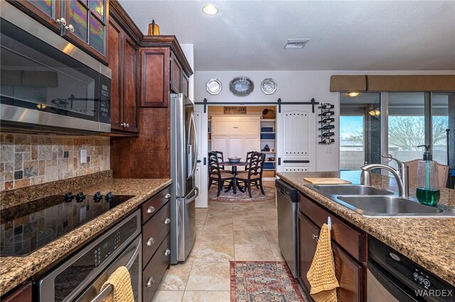 kitchen featuring tasteful backsplash, a barn door, visible vents, stainless steel appliances, and a sink