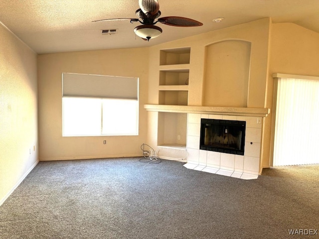 unfurnished living room featuring a textured ceiling, ceiling fan, built in features, vaulted ceiling, and a tiled fireplace