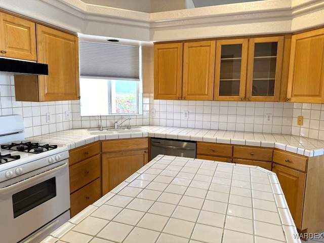 kitchen featuring tasteful backsplash, glass insert cabinets, white gas range, stainless steel dishwasher, and a sink