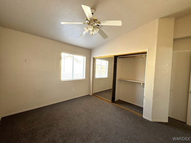 unfurnished bedroom featuring lofted ceiling, ceiling fan, a textured ceiling, a closet, and dark carpet