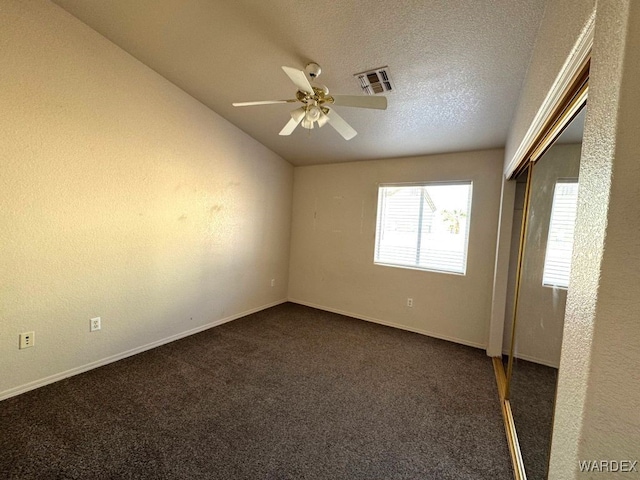 unfurnished room with a textured ceiling, visible vents, a ceiling fan, vaulted ceiling, and dark colored carpet