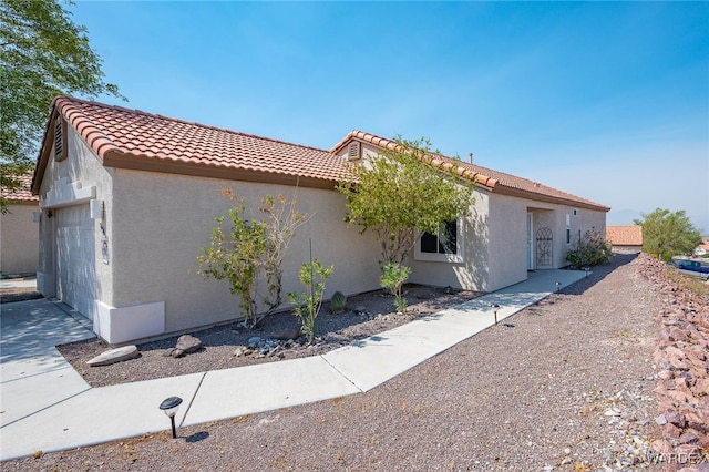 view of property exterior featuring an attached garage, a tiled roof, and stucco siding