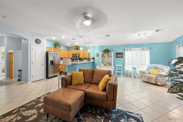 living area with light tile patterned floors, arched walkways, visible vents, a ceiling fan, and vaulted ceiling