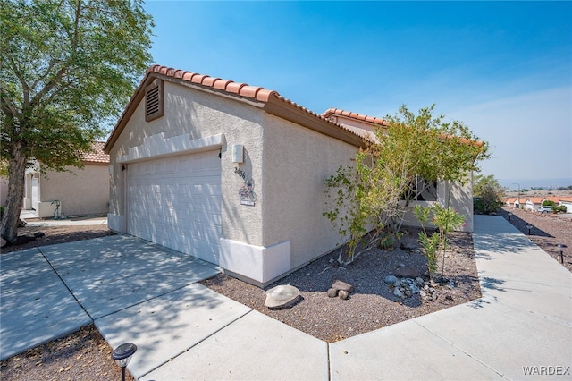 view of side of home featuring a tile roof, driveway, and stucco siding