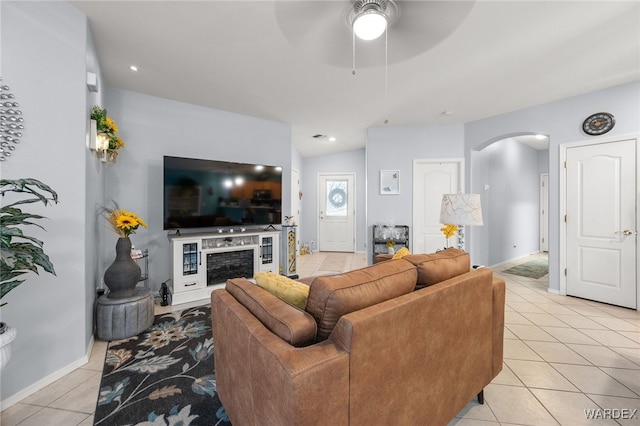 living room with arched walkways, ceiling fan, light tile patterned flooring, a fireplace, and baseboards