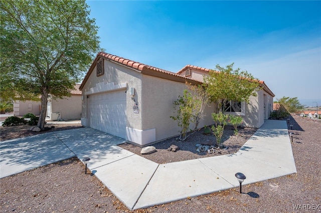 view of home's exterior featuring a garage, driveway, a tiled roof, and stucco siding