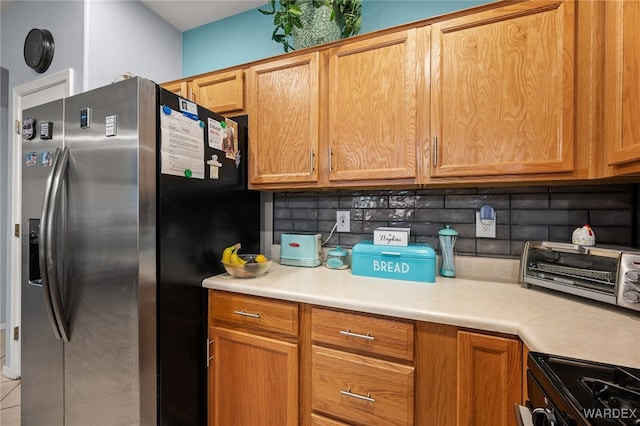 kitchen with light countertops, electric stove, backsplash, brown cabinetry, and stainless steel fridge