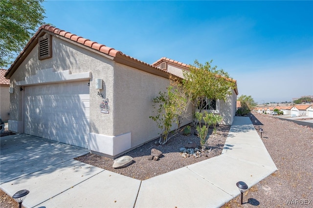 view of side of home featuring a garage, concrete driveway, a tile roof, and stucco siding