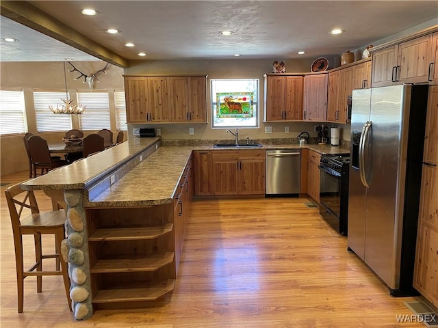 kitchen featuring stainless steel appliances, hanging light fixtures, a sink, a peninsula, and a kitchen breakfast bar