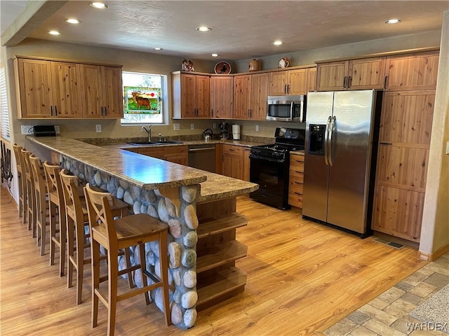 kitchen featuring a breakfast bar area, a peninsula, a sink, black appliances, and brown cabinetry