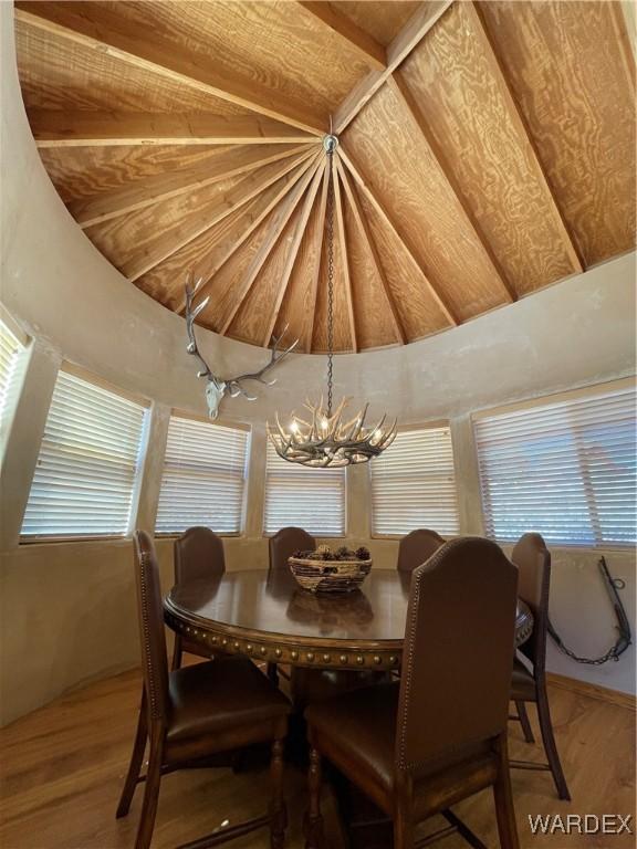 dining space with a chandelier, plenty of natural light, vaulted ceiling, and wood finished floors