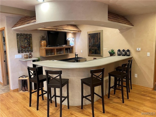 bar featuring indoor wet bar, light wood-style flooring, and baseboards