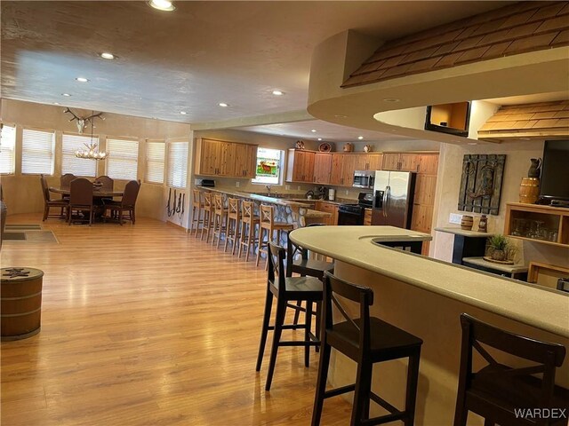 kitchen featuring recessed lighting, a kitchen breakfast bar, appliances with stainless steel finishes, brown cabinets, and light wood finished floors