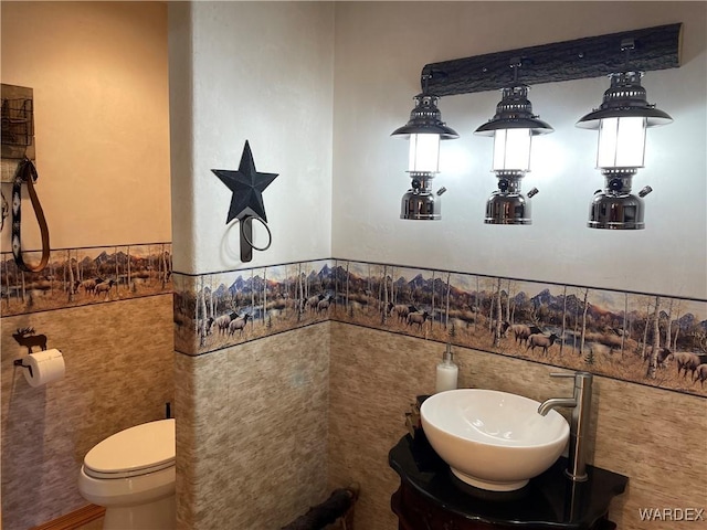 half bath with toilet, tile walls, a sink, and wainscoting