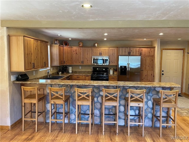 kitchen featuring a peninsula, a kitchen bar, appliances with stainless steel finishes, and a sink